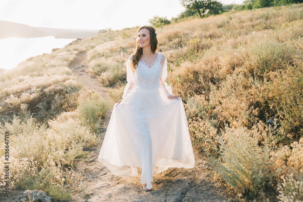 Bride in a luxurious white wedding dress in nature at sunset