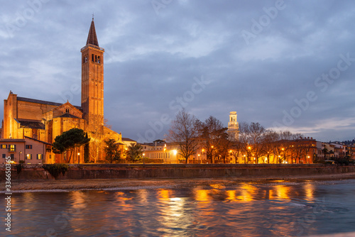 Night photo along the Adige river, Verona, Italy. Basilica of Santa Anastasia with the bell tower of the cathedral.