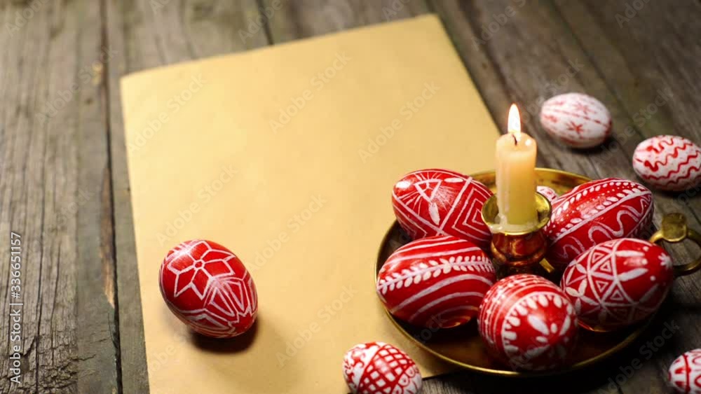 Red easter eggs with folk Ukrainian pattern lay on candlestick with burning candle stand on vintage paper on old wood background. Ukrainian traditional eggs pisanka and krashanka. Red easter eggs with folk Ukrainian pattern lay on candlestick with burning candle stand on vintage paper on old wood background. Ukrainian traditional eggs pisanka and krashanka.
