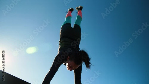 Young athletic girl does handstand and dismount in front of camera and sun