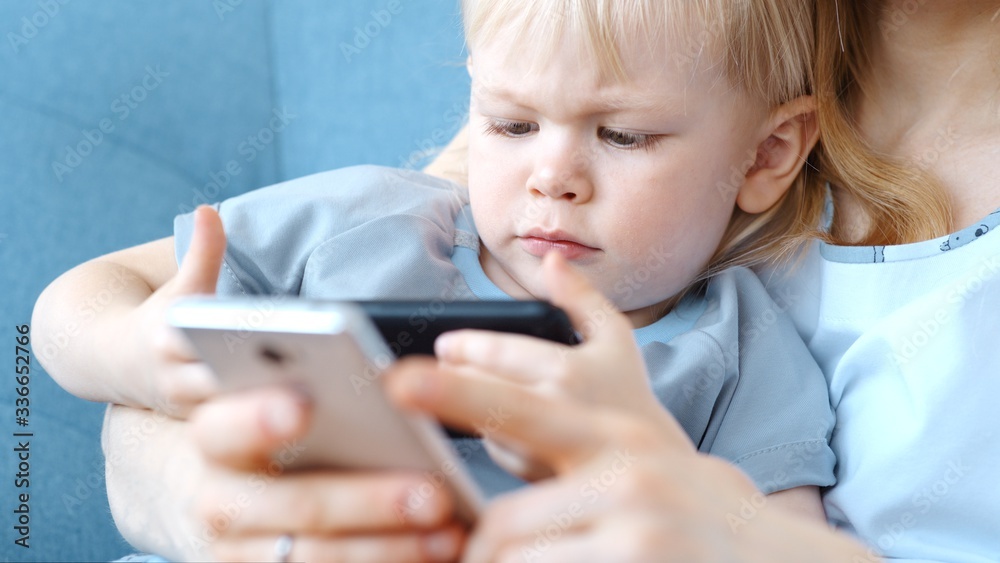 Young mother and son are enthusiastically engaged in online entertainment on a smartphone. Young mother and son are enthusiastically engaged in online entertainment on a smartphone.