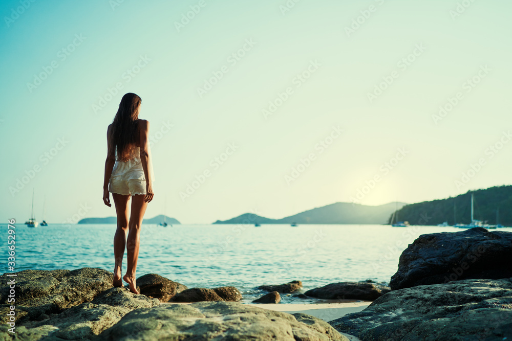 Young woman with long hear standing on sea beach enjoying the view.