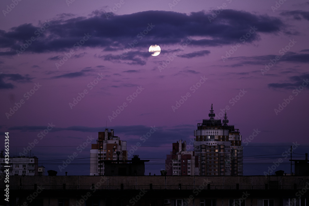Cityscape with full moon on blue night sky.