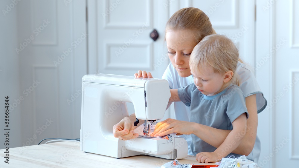Concept during self-isolation and quarantine. A woman with a small child sews a protective mask. Concept during self-isolation and quarantine. A woman with a small child sews a protective mask.