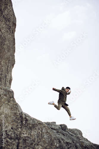 A young hipster man is jumping off a cliff