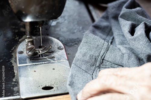 Foto Senior woman's stitching grey fabric on vintage sewing machine, Thread, Needle, Close up shot, Selective focus, Sewing process, Female's hobby
