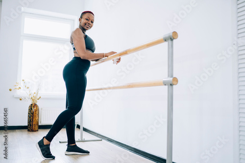 Smiling sportive female exercising on barre