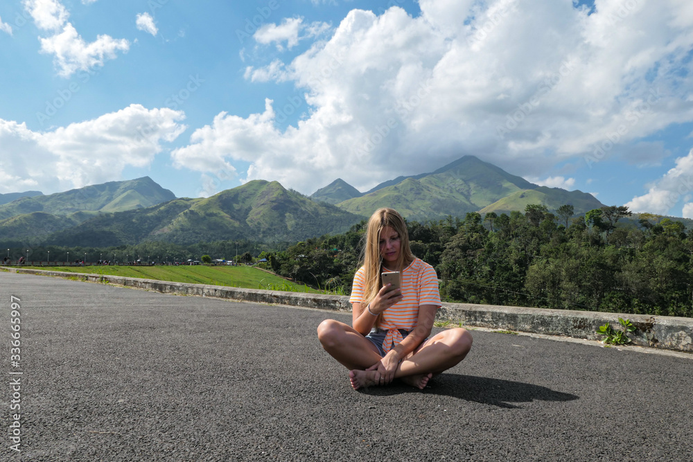 Girl sitting on the road to the mountains. Green mountains with blue sky and clouds. Girl in the nature.