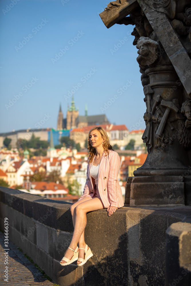 Young blonde woman walks along Charles Bridge in Prague in sunny day