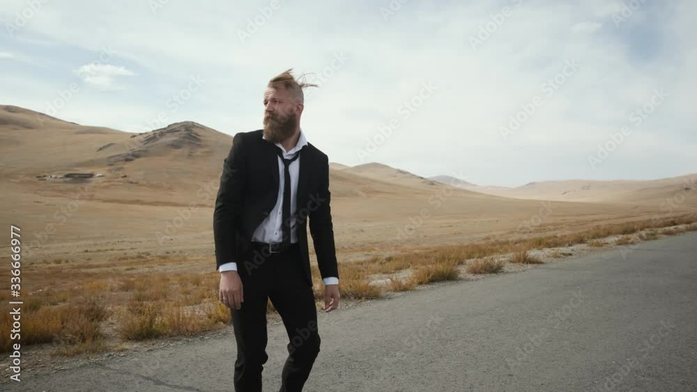 Caucasian man with beard and mustache in black suit with tie and white shirt, an office worker happy excited man walks with skateboard along an empty scenic mountain road 4k Caucasian man with beard and mustache in black suit with tie and white shirt, an office worker happy excited man walks with skateboard along an empty scenic mountain road 4k