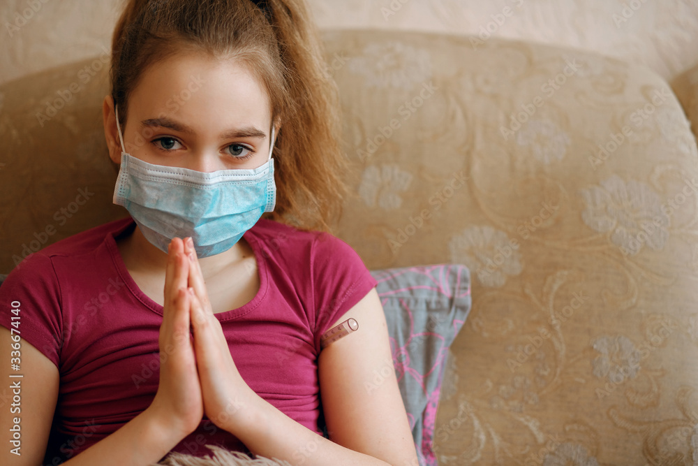 A girl in a protective mask against infection lies in bed and prays, an infected girl asks God for health, a coronovirus, the Coved-19 pandemic, a global epidemic, high body temperature, a thermometer