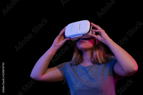 Chica con unas gafas de realidad virtual sobre un fondo negro y colores. Sujeta las gafas con las dos manos