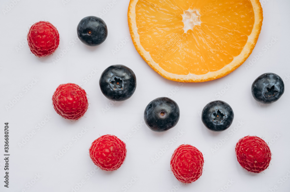juicy fresh berries blueberries and raspberries lie on a white table next to a slice of orange juicy fresh berries blueberries and raspberries lie on a white table next to a slice of orange