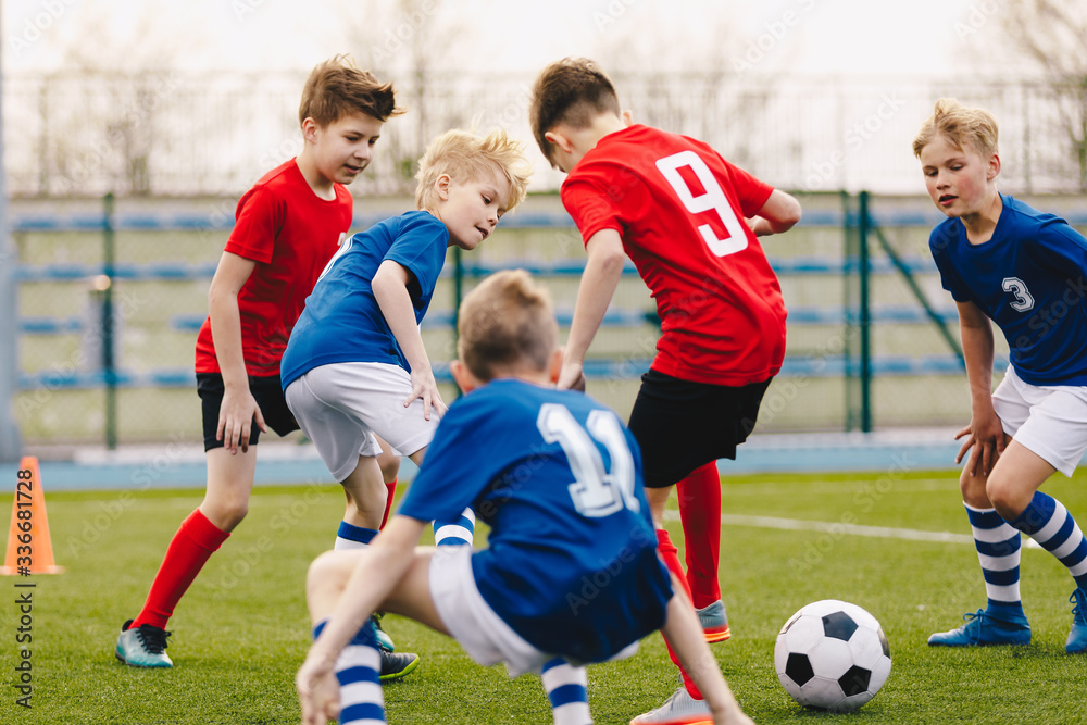 School boys playing football game. Young players kicking soccer ball on sports grass pitch. Happy children compete on a field School boys playing football game. Young players kicking soccer ball on sports grass pitch. Happy children compete on a field