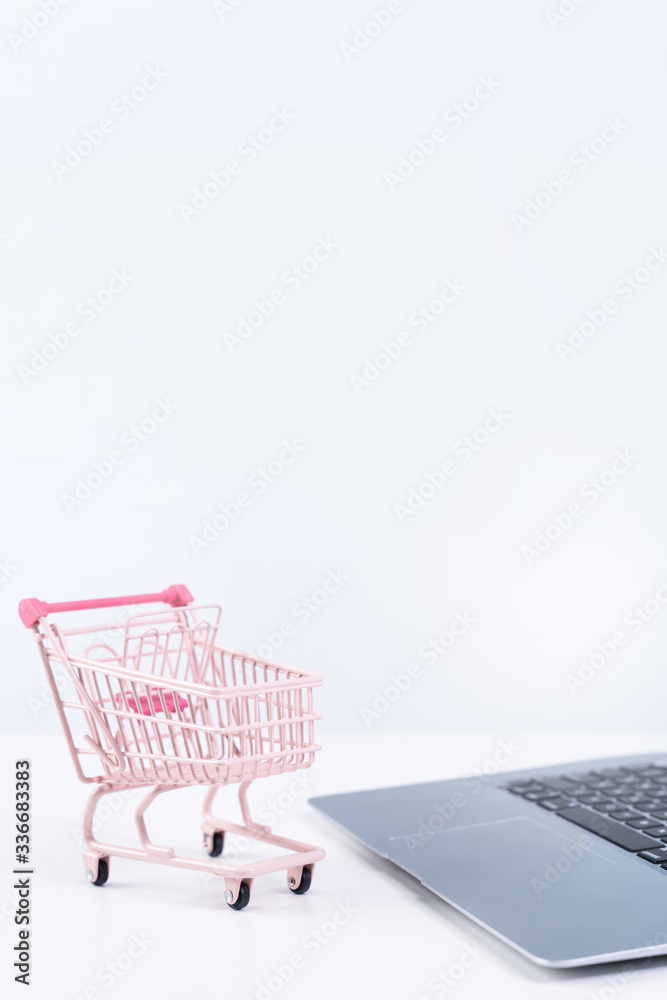 Online shopping. Mini empty pink shop cart trolley over a laptop computer on white table background, buying at home concept, close up