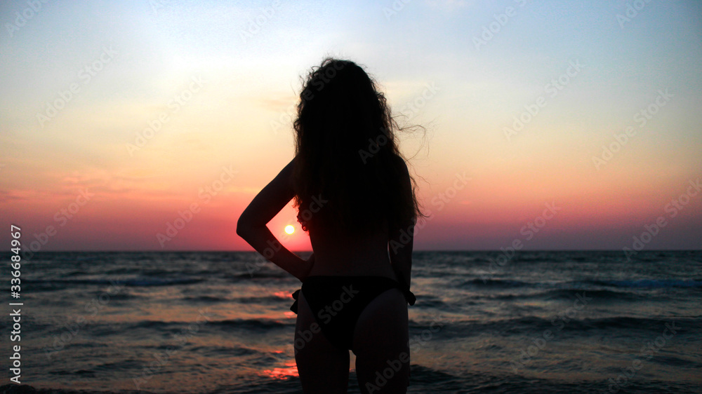 A curly girl standing in front of a sunset at the sea
