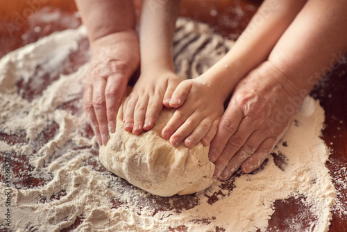 Female and children's hands holding a piece of dough. Female and children's hands knead the dough. Family weekend.