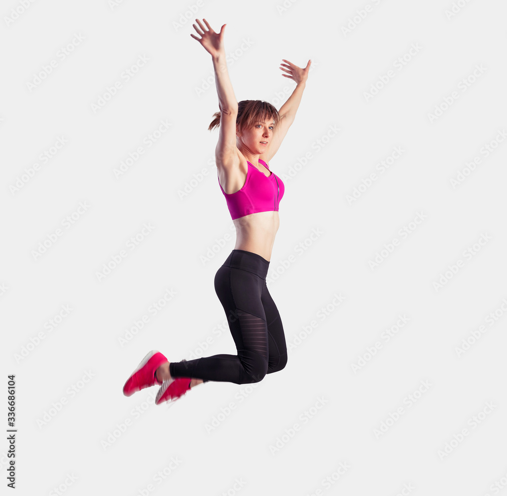 Happy joyful fitness woman in pink top and black leggings jumping over white background