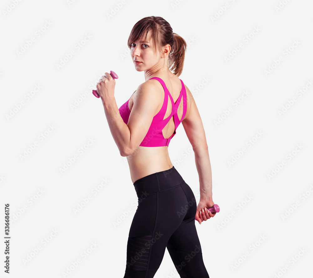 Sporty woman does the exercises with dumbbells on gray background. Photo of muscular woman in sportswear at studio Sporty woman does the exercises with dumbbells on gray background. Photo of muscular woman in sportswear at studio