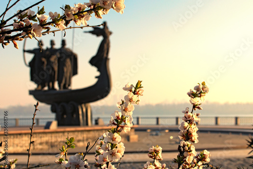 Beautiful white blossom flowers on tree branch in sunny spring morning. Blurred silhouette of Monument to legendary founders of Kyiv: Kiy, Schek, Khoryv and their sister Lybid in the background photo