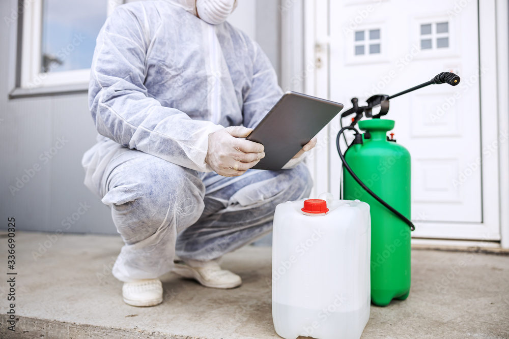 Φωτογραφία Man in virus protective suit and mask looking and typing on tablet, disinfecting buildings of coronavirus with the sprayer