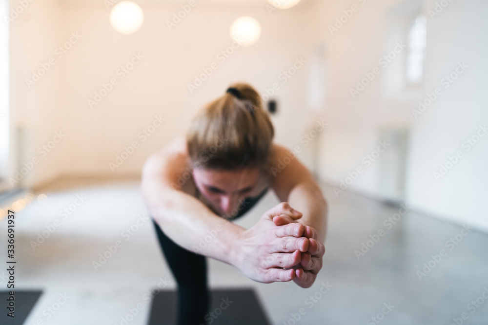 Fototapeta premium Beautiful young woman trains with yoga exercises in a white gym - Millennial in a moment of relaxation and personal well-being