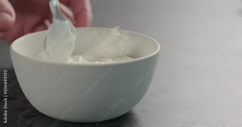 Slow motion man hand mix white yogurt in white bowl on concrete surface Slow motion man hand mix white yogurt in white bowl on concrete surface