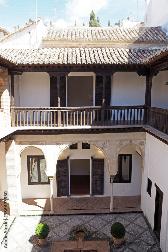 The part of the medieval stone Arabic house with columns, windows, the balcony with the wooden decorative wall, the tiled roof, flagging courtyard.