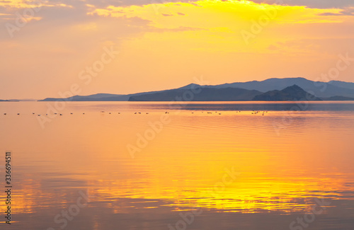 Magnificent spring morning landscape on shore of Baika Lake. Rising sun painted water of Small Sea in bright warm colors. Birds that arrived from winter are visible in distance. Natural background