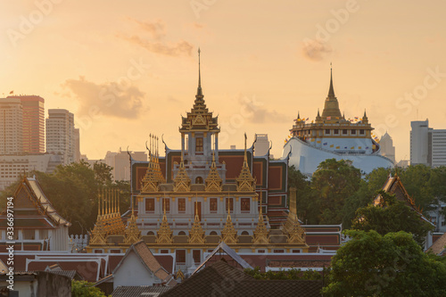 Loha Prasat Wat Ratchanatda and Golden Mountain pagoda, a buddhist temple or Wat Saket with skyscraper buildings in Bangkok Downtown, urban city at sunset, Thailand. Thai Landmark. Architecture. photo