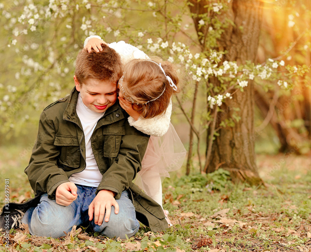 Fototapeta premium Native cheerful elder brother and little sister have fun in spring park where blossoming cherry flowers in a botanical garden. Family day. Brother and sister day. Children Protection Day. Easter