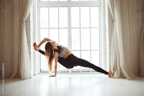 Young skinny woman doing yoga against window in her home during quarantine. What to do at home during self-isolation. Stay home