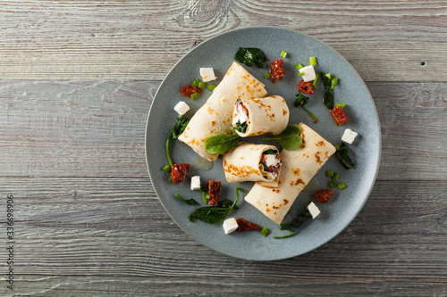 Pancakes with spinach, feta and dried tomatoes. Served on a gray plate. Wooden natural background.