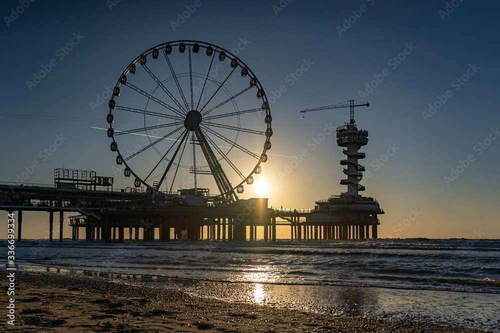 The setting sun is just above the Pier in Scheveningen and glistens in the wet sand on the water line of the North Sea