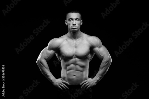 Muscular model sports young man in jeans showing his press on a black background. Fashion portrait of sporty healthy strong muscle guy. Sexy torso. Black and white photography 