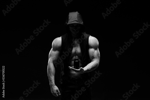Muscular bodybuilder with jar of protein on a dark background. Sports nutrition. Bodybuilding nutrition supplements, sport, workout, healthy lifestyle concept. Black and white photography