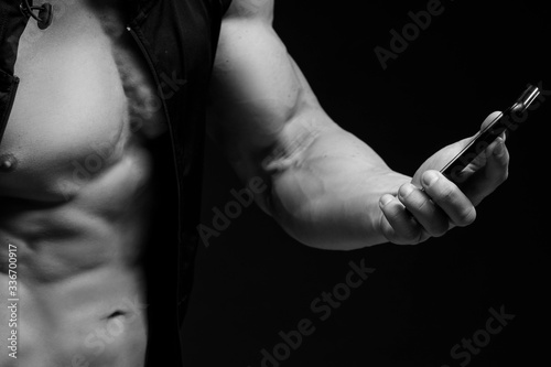 Muscular bodybuilder with phone in hands on a dark background. Sports nutrition. Bodybuilding nutrition supplements, sport, workout, healthy lifestyle concept. Black and white photography