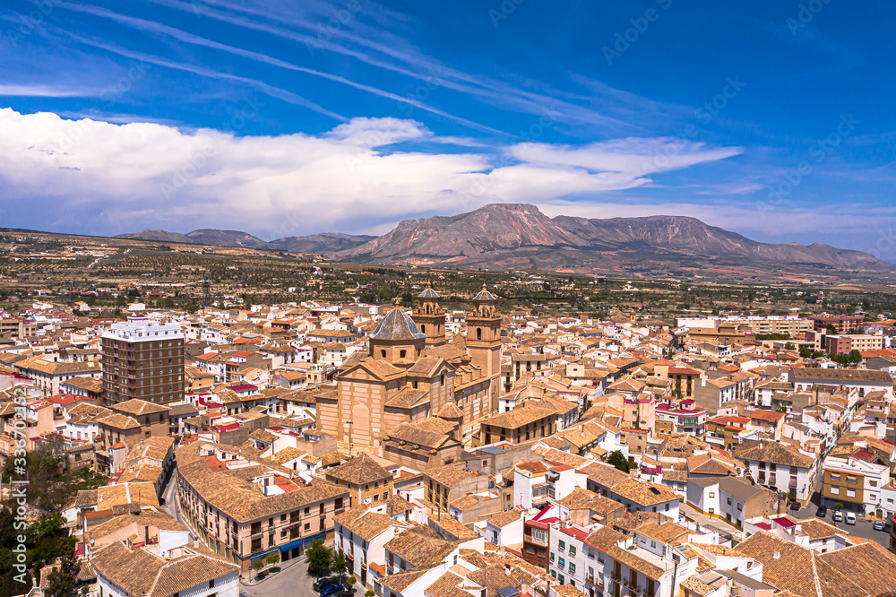Aerial Drone photo of a beautiful city in a Almeria, Andalucia, Spain called Velez Rubio with red and orange house roof tops and a beautiful cathedral in the heart of the town with blue sky & mountain