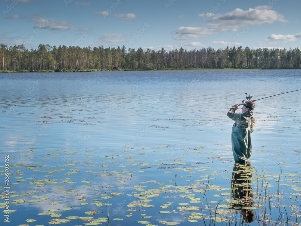 Obraz premium Karelia, Vodlozero - 29.07.2019: Young man fishing with spinning in lake. Ecotourism, visiting fragile, pristine, undisturbed natural areas. Active holidays in Karelia. Portrait