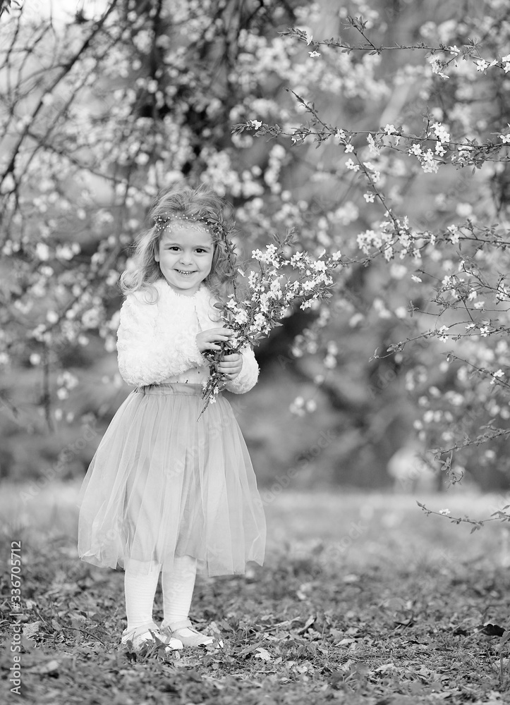 Stunning black and white portrait little girl laughs and has fun in a flying skirt and a fur blouse with a bouquet of blossoming cherry flowers in a spring garden. Daughter's day. Easter Stunning black and white portrait little girl laughs and has fun in a flying skirt and a fur blouse with a bouquet of blossoming cherry flowers in a spring garden. Daughter's day. Easter