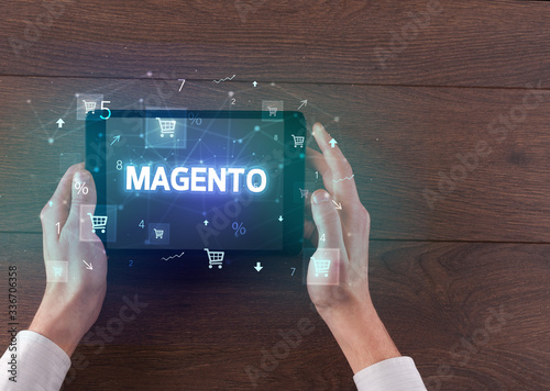 Close-up of a hand holding tablet with MAGENTO inscription, online shopping concept photo