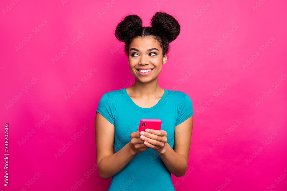 Photo of funny youngster dark skin lady two buns hold telephone hands look side empty space interested wear blue casual t-shirt isolated magenta color background - obrazy, fototapety, plakaty 