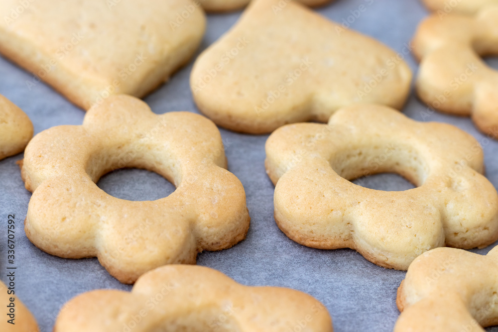 Baked shortbread cookies in the form of flowers and hearts on a baking sheet with parchment paper just taken out of the oven. Tea snack for breakfast. Selective focus. Closeup view Baked shortbread cookies in the form of flowers and hearts on a baking sheet with parchment paper just taken out of the oven. Tea snack for breakfast. Selective focus. Closeup view