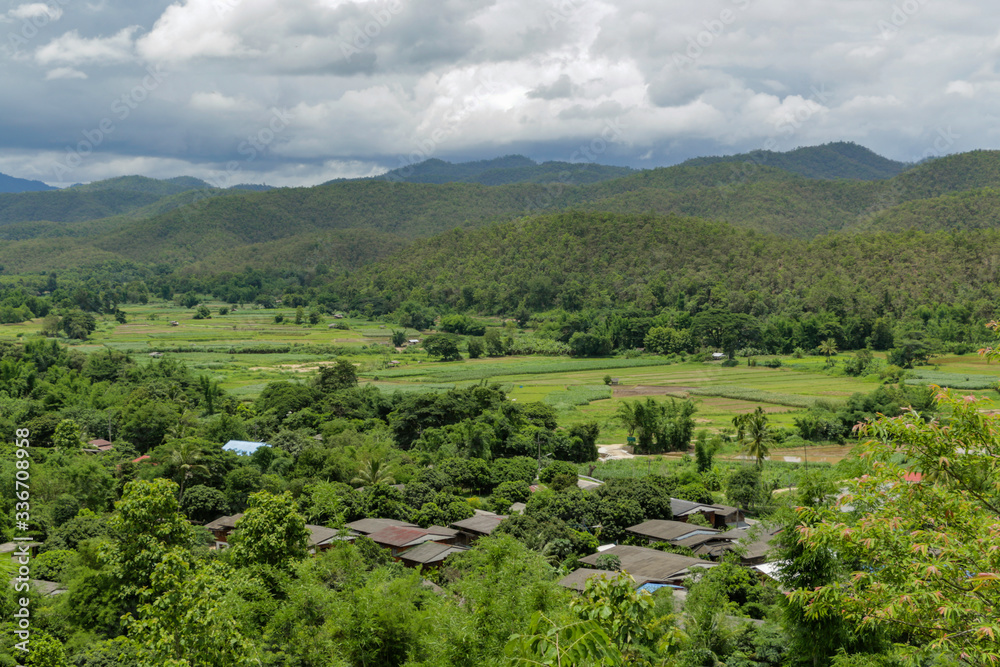 Panoramic hilly landscape of tropical forest mixed with residential area and farm plots. It shows different land use and green plantations.