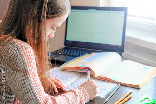 Girl sitting at desk doing lessons with notebook near laptop