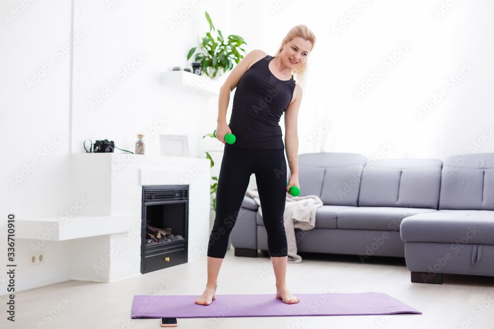 Obraz premium a thin European girl doing stretching exercises at home on a yoga mat, rays of light shine from the window. flare. quarantine sport.