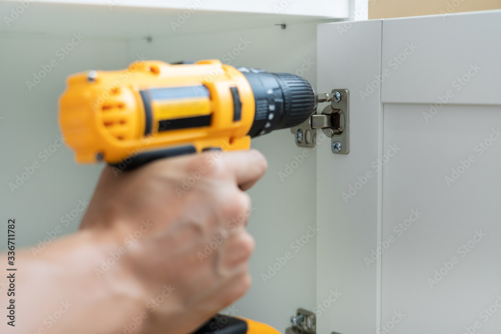 close up man holding cordless screwdriver machine and screws lie for screwing a screw assembling furniture at home.