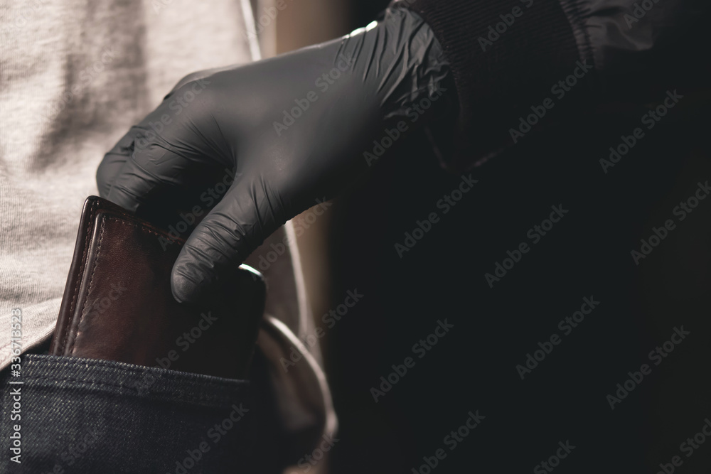 wallet money. Close up of a the hand of thief Pickpocket stealing a purse from the back jeans pocket of a man walking outdoors on a road night dark background. Crime in an economic downturn concept. wallet money. Close up of a the hand of thief Pickpocket stealing a purse from the back jeans pocket of a man walking outdoors on a road night dark background. Crime in an economic downturn concept.