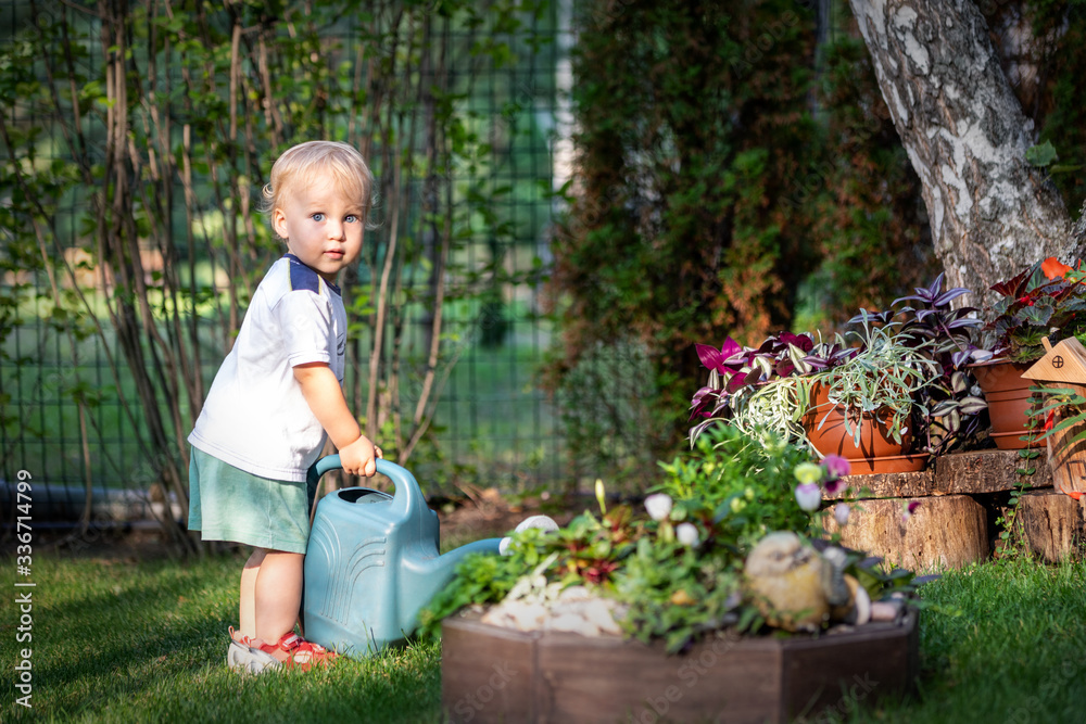 Cute adorable caucasian blond little toddler boy in watering flowerbed flower pot with green plastic can outdoors. Fun baby boy gardening plant at backyard countryside cottage on bright summer day Cute adorable caucasian blond little toddler boy in watering flowerbed flower pot with green plastic can outdoors. Fun baby boy gardening plant at backyard countryside cottage on bright summer day