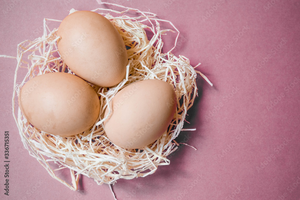 Decorative Easter composition for a postcard. Three chicken farm unpainted fresh eggs in a decorative sisal nest on a light pink background with a close-up copy space, top view Decorative Easter composition for a postcard. Three chicken farm unpainted fresh eggs in a decorative sisal nest on a light pink background with a close-up copy space, top view